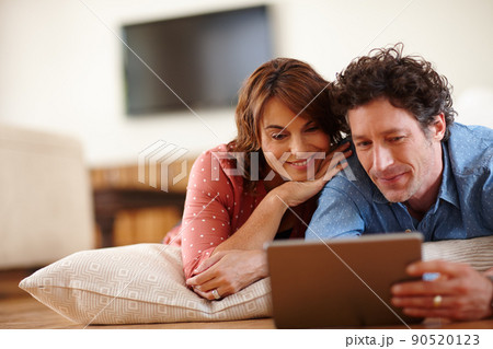 Time to unwind online. Shot of a husband and wife using a digital tablet together at home. 90520123