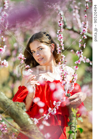 Woman in red dress standing near blooming peach tree 90520494