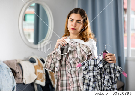 Young woman chooses shirts from her home wardrobe Young woman chooses shirts from her home wardrobe 90520899