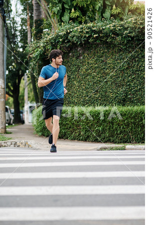 Its safe to cross. Shot of a sporty young man running across a road as exercise outside during the day. Its safe to cross. Shot of a sporty young man running across a road as exercise outside during the day. 90521426