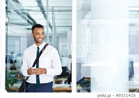 Feeling at home in his work domain. A handsome young african american businessman using his smartphone while in the office. 90521428