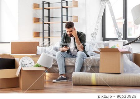 sad man with smartphone and boxes moving home sad man with smartphone and boxes moving home 90523928