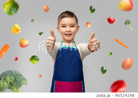 smiling boy in apron showing thumbs up over food 90524298