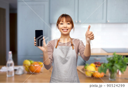 happy woman in apron showing smartphone in kitchen 90524299