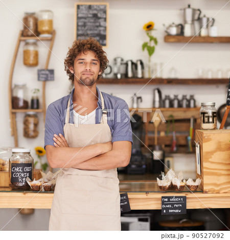 Always a friendly face at the cafe. Portrait of a male barista standing happily at a cafe counter. Always a friendly face at the cafe. Portrait of a male barista standing happily at a cafe counter. 90527092