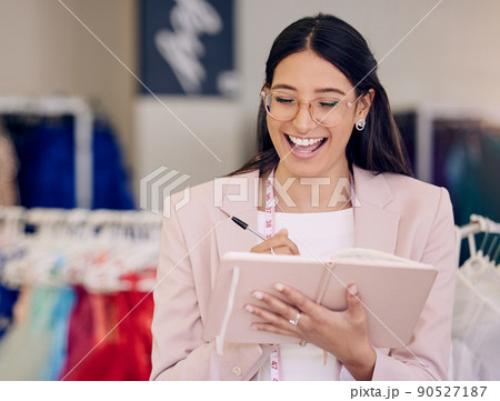 Nothing feels better than being fully booked. Shot of an attractive young seamstress writing notes while working in her boutique. Nothing feels better than being fully booked. Shot of an attractive young seamstress writing notes while working in her boutique. 90527187