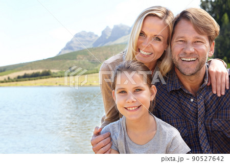 Memories to last a lifetime. Portrait of a happy family of three sitting together at a lake. 90527642