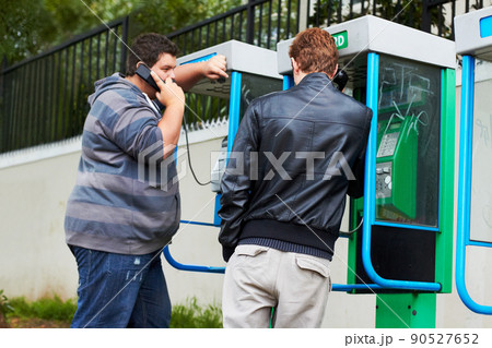 Phoning home. Two young men making phone calls from public pay-phone booths. 90527652