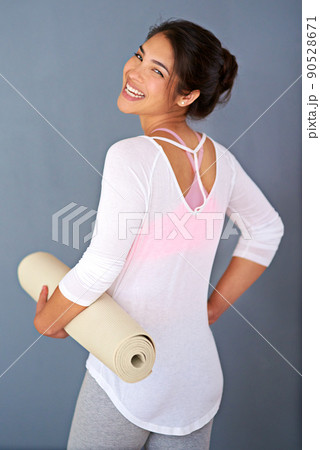 My mat is my canvas and yoga my art. Rearview shot of a sporty young woman holding her yoga mat against a grey background. 90528671