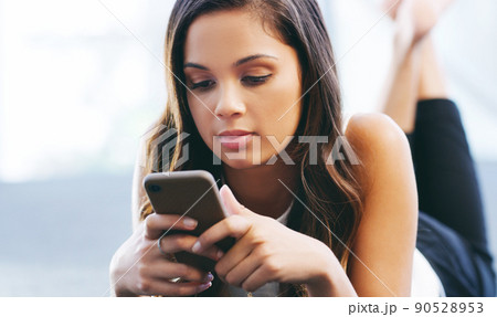 I wish I was there. Shot of a young woman laying on the floor and using a smartphone. I wish I was there. Shot of a young woman laying on the floor and using a smartphone. 90528953