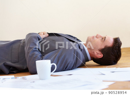 Work really takes its toll. A handsome young businessman lying on the floor of his office. 90528954