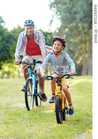 Enjoying a day out with dad. Shot of a father and son riding bicycles in a park. 90528999