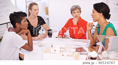 Discussing the blueprints for their new project. A group of female architects working together on a project at a conference table. Discussing the blueprints for their new project. A group of female architects working together on a project at a conference table. 90529767