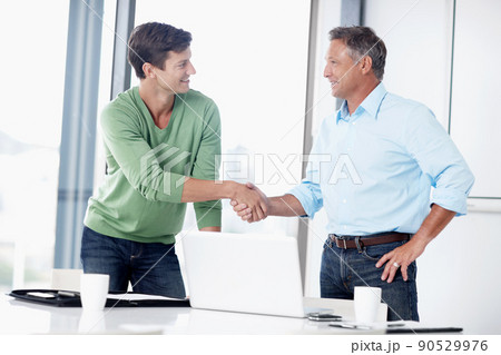 We make a good team. A mature executive shaking the hand of his younger colleague. We make a good team. A mature executive shaking the hand of his younger colleague. 90529976