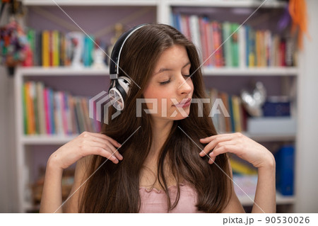 A teenager listens to music with her eyes closed and a bookcase with books in the tel. A teenager listens to music with her eyes closed and a bookcase with books in the tel. 90530026