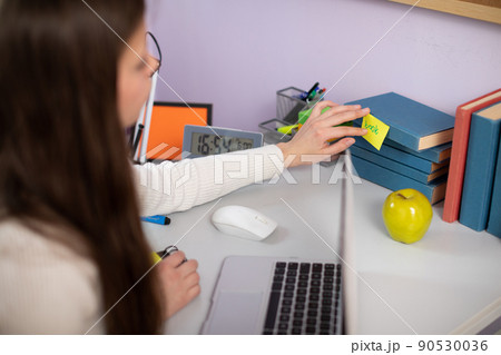 A young brunette girl sticks a note on a book while learning English. A young brunette girl sticks a note on a book while learning English. 90530036
