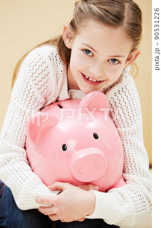 I always save my pocket money. Cropped portrait of a cute little girl smiling while holding a piggybank. 90531226