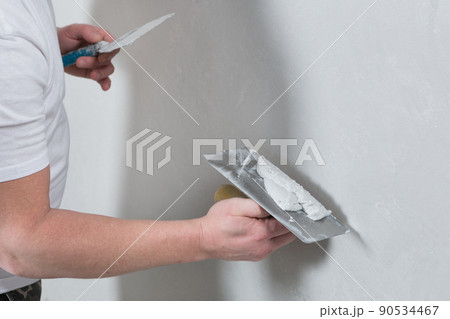 the master holds a spatula with a mortar in his hand, applying decorative plaster to the wall 90534467