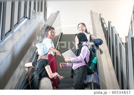 Group of young female students laughing while going up the escalator. 90534837