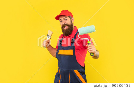 happy man in work clothes hold paint roller and brush on yellow background 90536455