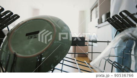 Young woman taking out clean dishes from a dishwasher machine in kitchen. Cleaning, housework, housewife. 90536766