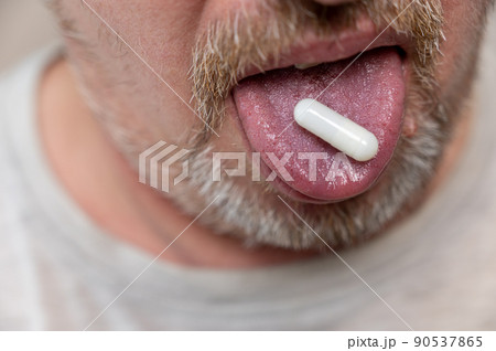 A man takes medication. The lower part of the man's face. The white pill is on his tongue. Mature man with stubble. Gray hair on his beard and mustache. Close-up. Selective focus. A man takes medication. The lower part of the man's face. The white pill is on his tongue. Mature man with stubble. Gray hair on his beard and mustache. Close-up. Selective focus. 90537865