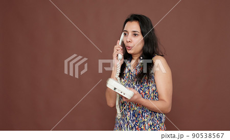 Indian woman using landline phone call to have remote conversation with people in studio. Being busy talking on telephone line after dialing number, chatting remotely over background. 90538567