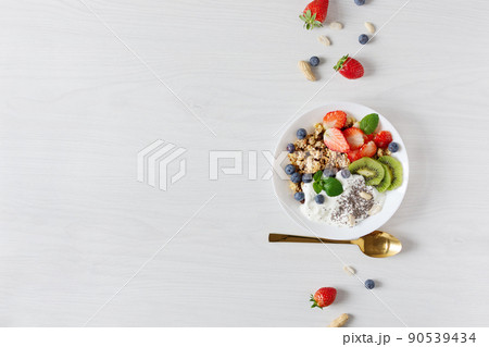 White ceramic bowl of homemade granola with yogurt, fresh berries and fruits on white wooden table background top view. White ceramic bowl of homemade granola with yogurt, fresh berries and fruits on white wooden table background top view. 90539434