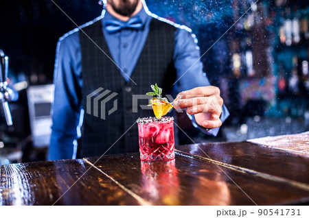 Focused barkeeper adds ingredients to a cocktail at the bar counter 90541731