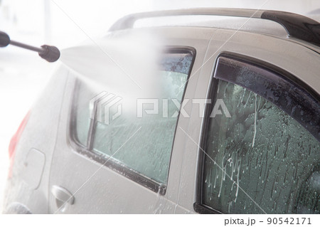 A process of flushing soap sud on silver car window with pressurised water stream at self-service indoor car wash station 90542171