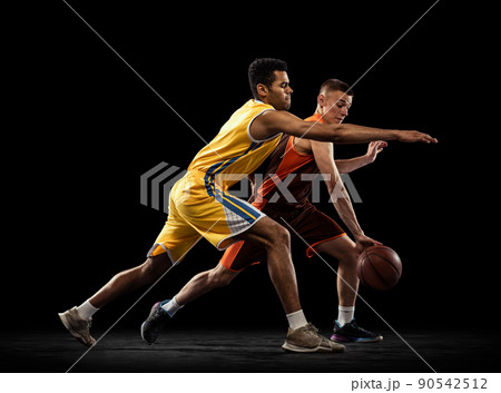 Portrait of two sportive men, basketball players in uniform playing, training isolated on black studio background. Following the ball carrier. Portrait of two sportive men, basketball players in uniform playing, training isolated on black studio background. Following the ball carrier. 90542512