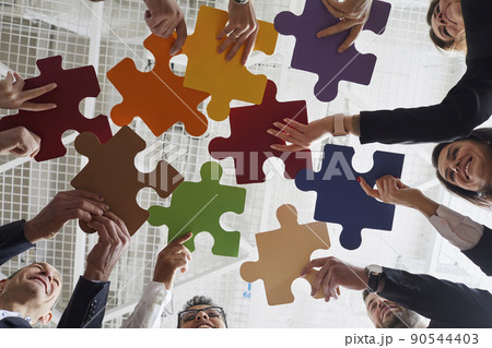Joyful male and female office workers put together colored pieces of puzzle at meeting in office. Joyful male and female office workers put together colored pieces of puzzle at meeting in office. 90544403