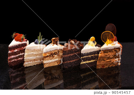 Assorted large pieces of different cakes: chocolate, raspberries, strawberries, nuts, blueberries. Pieces of cakes on a black table. 90545457