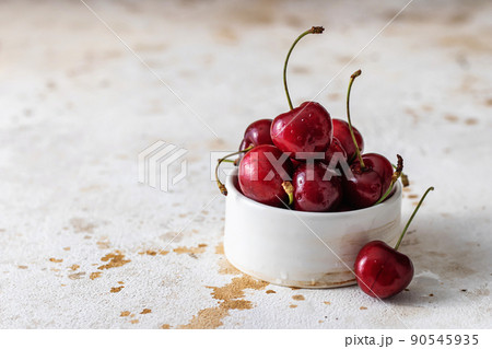 Fresh cherries close up in white ceramic bowl on textured background, copy space 90545935