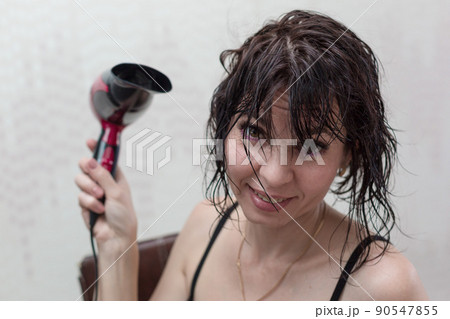 Young woman getting ready for a date, drying her head with a hair dryer in front of a mirror Young woman getting ready for a date, drying her head with a hair dryer in front of a mirror 90547855