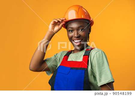 Young african american woman wearing architect hardhat against yellow background Young african american woman wearing architect hardhat against yellow background 90548199