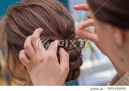 Women's fingers gently insert the hairpin into the client's hair. 90549889
