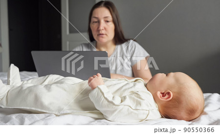 Mother freelancer looks after baby girl working on laptop 90550366