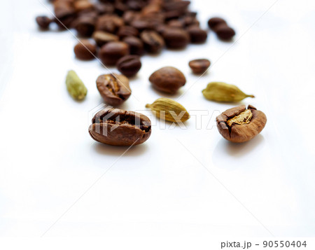 Coffee beans and cardamom grains are scattered on a white glossy surface. Coffee beans and cardamom grains are scattered on a white glossy surface. 90550404