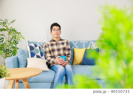 カップを持ってソファーでリラックスする男性 カップを持ってソファーでリラックスする男性 90550735