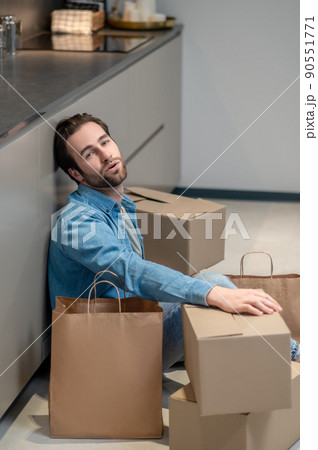 Man looking at camera sitting on floor near boxes Man looking at camera sitting on floor near boxes 90551771