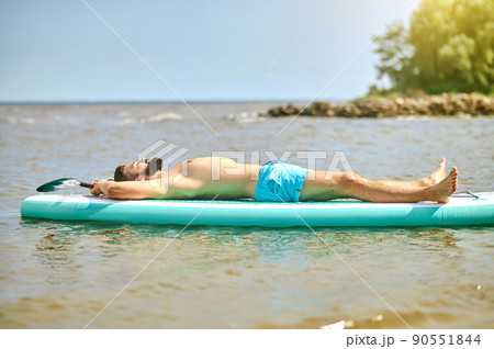 A man in blue swim wear lying on a kaya and sunbathing A man in blue swim wear lying on a kaya and sunbathing 90551844