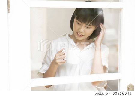 ガラス格子のドアから外を見る若い女性 90556949