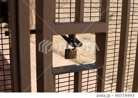 Padlock hangs on an iron closed gate with peeling paint and rust 90559993