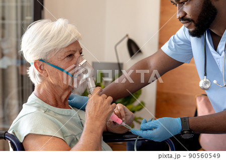 African american male health worker helping caucasian senior woman to use oxygen mask African american male health worker helping caucasian senior woman to use oxygen mask 90560549