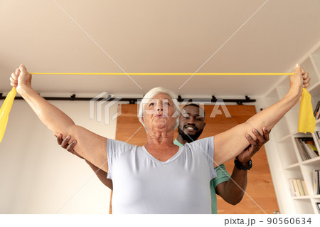 African american male physiotherapist helping senior woman to exercise with resistance bands 90560634