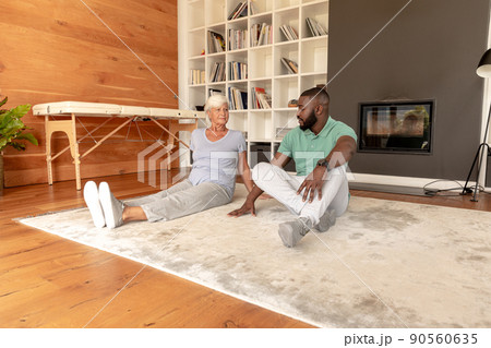 African american male physiotherapist and caucasian senior woman sitting on the floor at home African american male physiotherapist and caucasian senior woman sitting on the floor at home 90560635