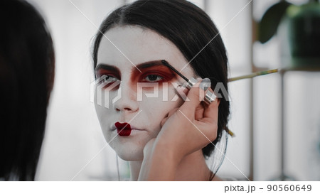 Close-up A young woman creates the image of a geisha for a girl. Makeup. Creating an image for an event Close-up A young woman creates the image of a geisha for a girl. Makeup. Creating an image for an event 90560649