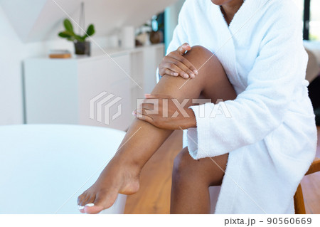 Mid section of woman in a bathrobe applying moisturizer on her leg sitting near bath tub Mid section of woman in a bathrobe applying moisturizer on her leg sitting near bath tub 90560669