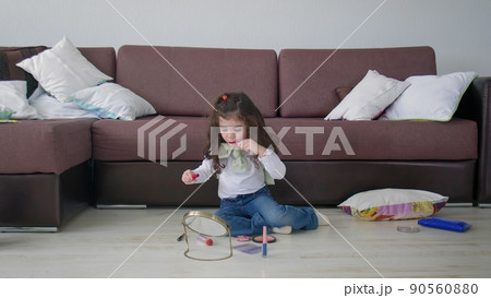 A little girl sits on the floor in a room and plays with makeup. Beauty and fashion 90560880
